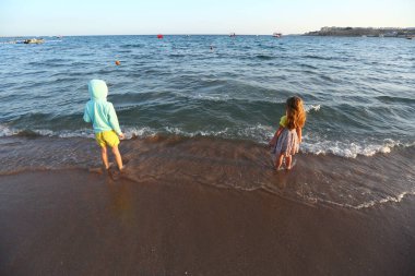 Sahilde duran iki çocuğun günbatımı portresi.