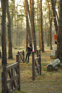 Sonbahar ormanında iple havada uçan bir çocuğun portresi, emniyet kemeri takıyor.