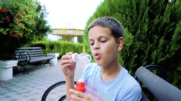 Щасливий підліток дме мильні бульбашки у весняному парку . — стокове відео