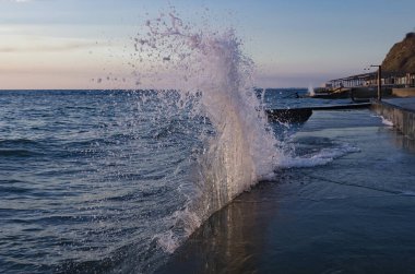 Altında belgili tanımlık deniz dalgaları sıçraması ve taşlar ile parlak günbatımı.