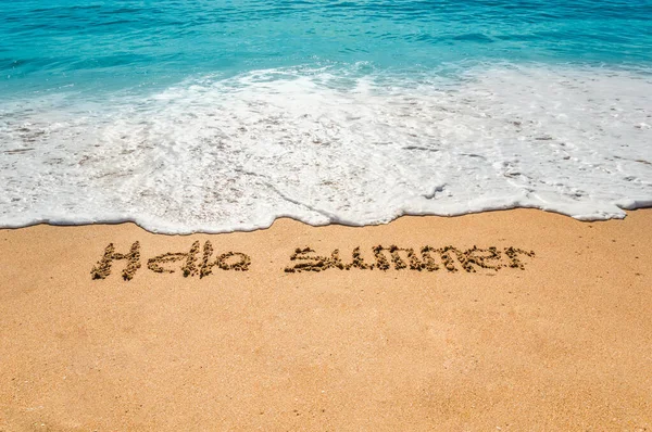 Testo scritto a mano ciao estate sulla sabbia dorata della spiaggia con onde in arrivo — Foto Stock