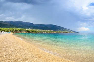 Pebble beach Zlatni Rat or Golden Horn in Bol, Brac Island, Croatia. Scenic gravel beach, mountain and turquoise sea water