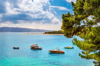 Boats near Zlatni Rat or Golden Horn beach in Bol town on Brac Island, Croatia. Scenic pebble beach with pine trees and turquoise sea water
