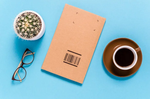 Mavi arka planda kutu paket kahve fincanı, gözlük ve kaktüs vardı. Mal göndermek ya da almak. Sevkiyat ve teslimat kavramı.