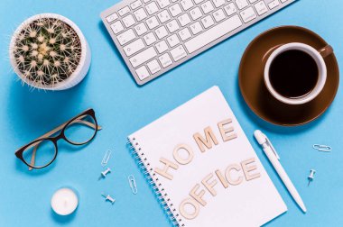 Modern çalışma alanı, klavye, kahve fincanı, not defteri, kalem, gözlük ve kaktüs mavi arka planda. Mektuplarda İçişleri Bakanlığı yazıyor. Üst görünüm