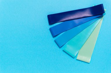 Mavi, turkuaz ve yeşil renkli elastik lastik direnç bantları. Spor aletleri ya da evde spor yapmak için. Fitness ve rehabilitasyon ekipmanları. Düz yatıyordu