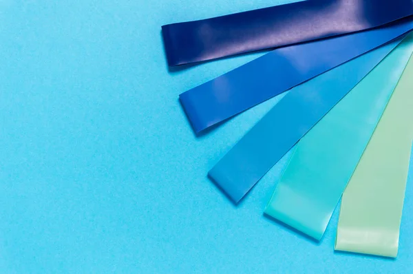 Mavi, turkuaz ve yeşil renkli elastik lastik direnç bantları. Spor aletleri ya da evde spor yapmak için. Fitness ve rehabilitasyon ekipmanları. Düz yatıyordu