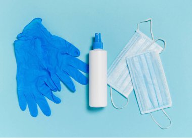 Tıbbi maske, dezenfektan ya da el dezenfektanı ve mavi arka planda tek kullanımlık eldivenler.