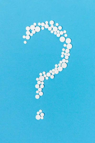 Mavi arka planda soru işareti şeklinde beyaz haplar. İlaç ya da tıbbi konsept, ilaç seçimi ya da hastalık tedavisinde belirsizlik, faq. Coronavirus ilacı.