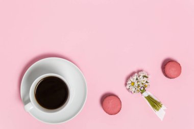 Beyaz kahve, iki pembe Fransız badem kurabiyesi ve pembe arka planda bir demet papatya çiçeği. Güzel romantik kahvaltıya yakın çekim. Üst görünüm, kopyalama alanı olan düz uzanma