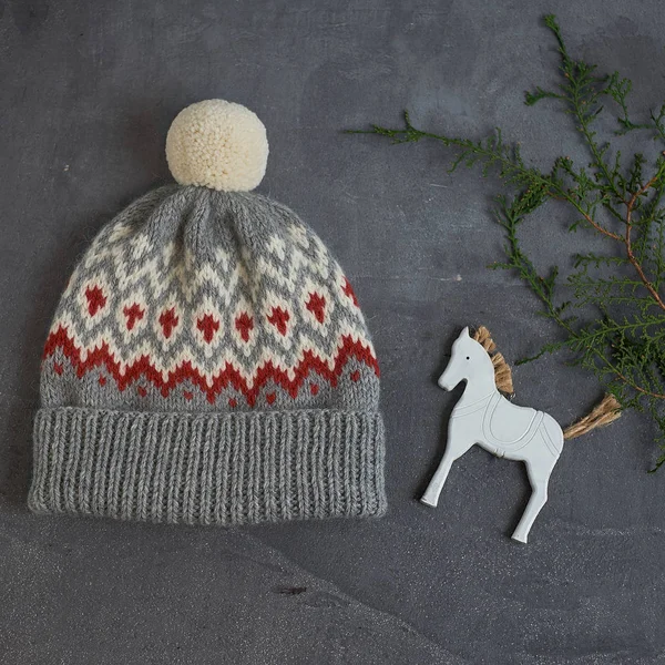 Sombrero de invierno gris con un patrón jacquard sobre un fondo gris con un caballo de madera —  Fotos de Stock