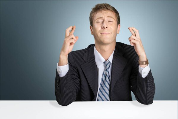 businessman sitting at table with fingers crossed