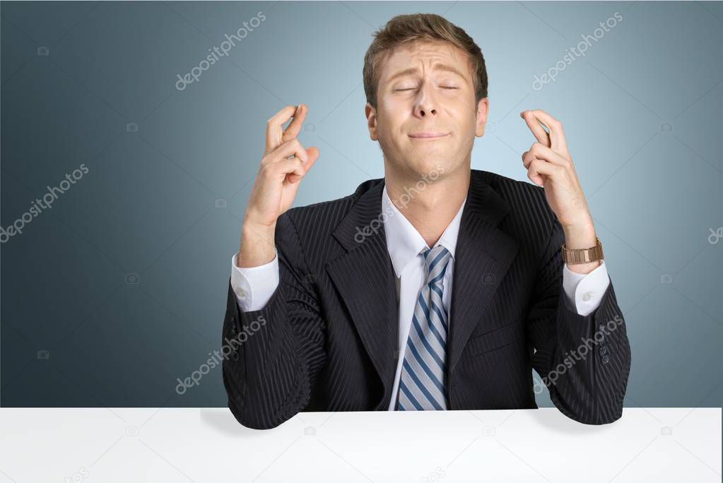 businessman sitting at table with fingers crossed