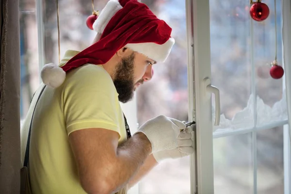 Человек в шляпе Санты ремонтирует окно — стоковое фото