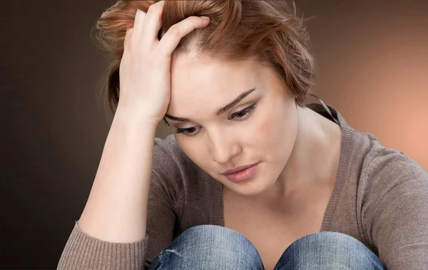 Worried woman sitting holding knees — Stock Photo, Image