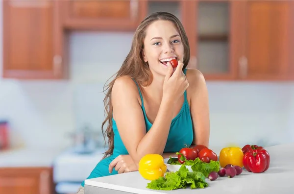 Jovem mulher comer legumes na cozinha — Fotografia de Stock