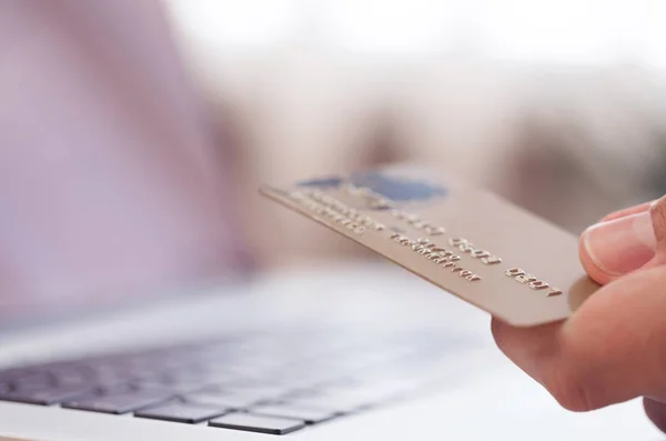 hand holding credit card near laptop