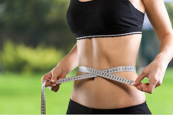 Молодая женщина измеряет свою тонкую талию
 
