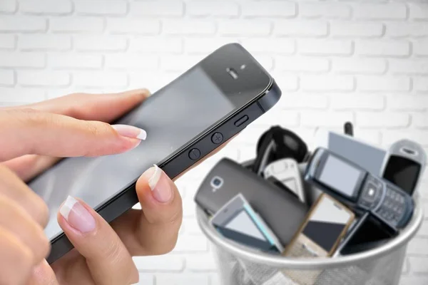 hand with phone and rubbish bin full of old cellphones