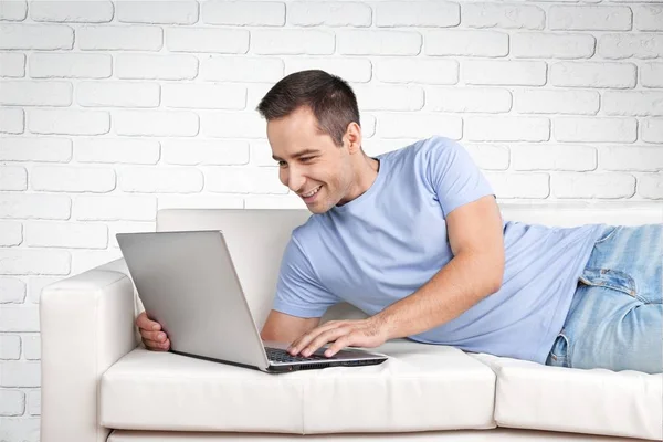 Homem relaxante no sofá com um laptop — Fotografia de Stock