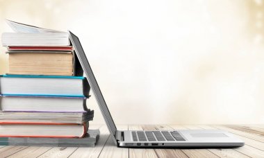 Tahta masada dizüstü bilgisayarı olan bir yığın kitap. 