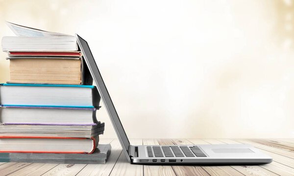 Стопка книг с ноутбуком на деревянном столе
 