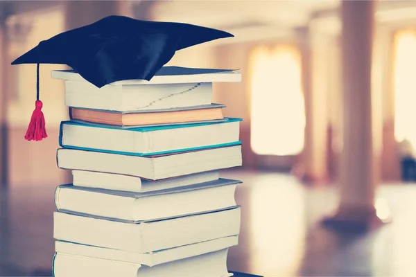 Graduiertenmütze Und Bücherstapel Auf Verschwommenem Hintergrund — Stockfoto