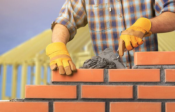 Рабочий возводит кирпичную стену в доме
