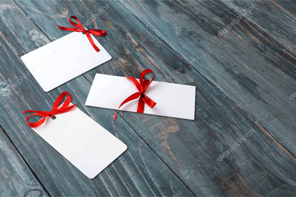 close-up of greeting cards with red ribbons on wooden table 