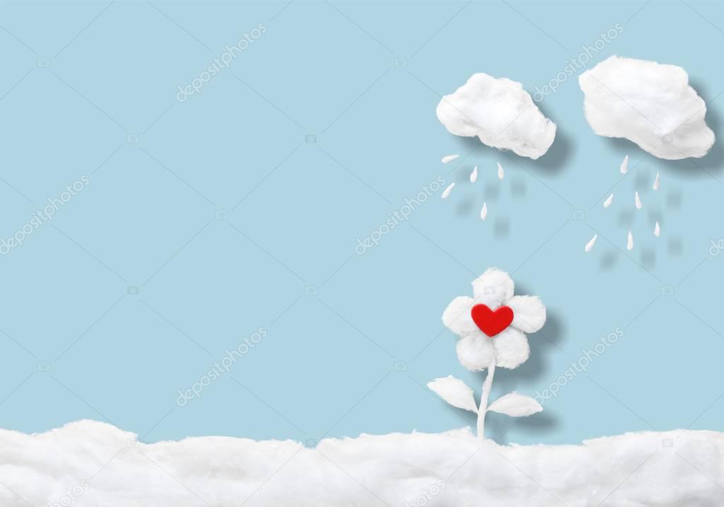 Two small clouds pouring rain over flower, in a heavenly scenery where the clouds are made from cotton-wool, on a blue sky paper background.
