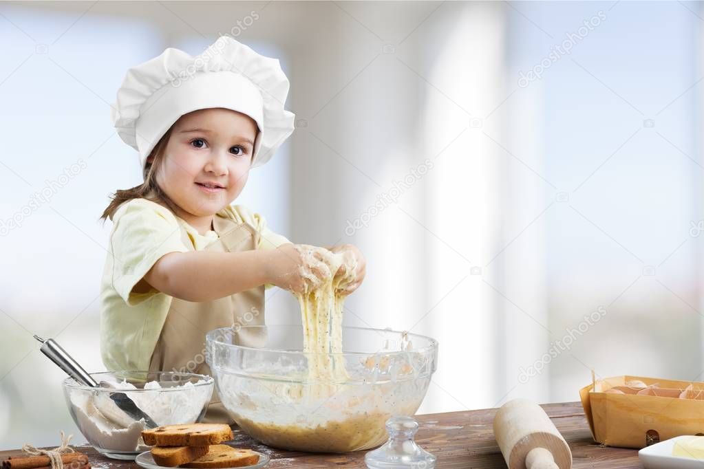 Little girl Cooking with dough on blurred kitchen background