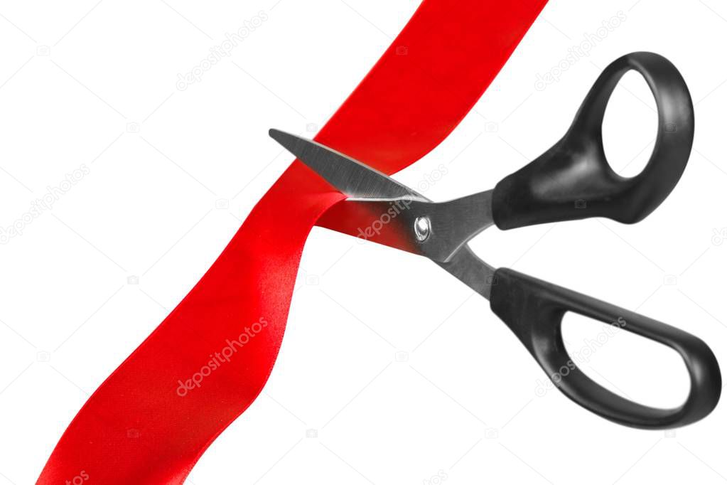 Scissors cutting red ribbon, close-up view on  background