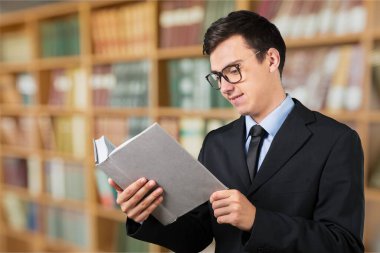 Genç adam kütüphanede kitap okuyor.