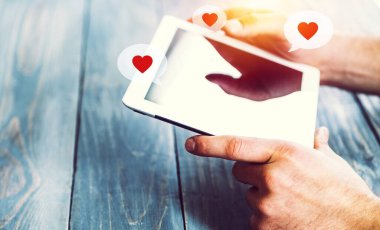 Ahşap kalasların arkasında kalpler olan bir tableti tutan eller.