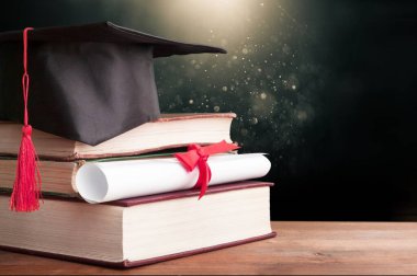 Mezuniyet şapkası ve tahta masa üzerinde kitapları olan bir diploma.