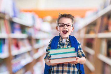Kütüphanede kitapları olan gözlüklü şirin bir çocuğun portresi.