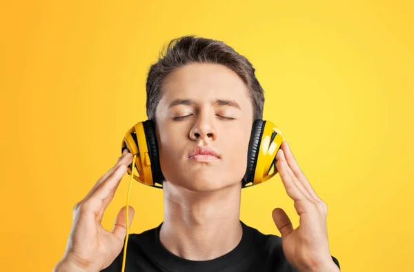 黄色の背景でヘッドフォンで音楽を聴いている若者は — ストック写真