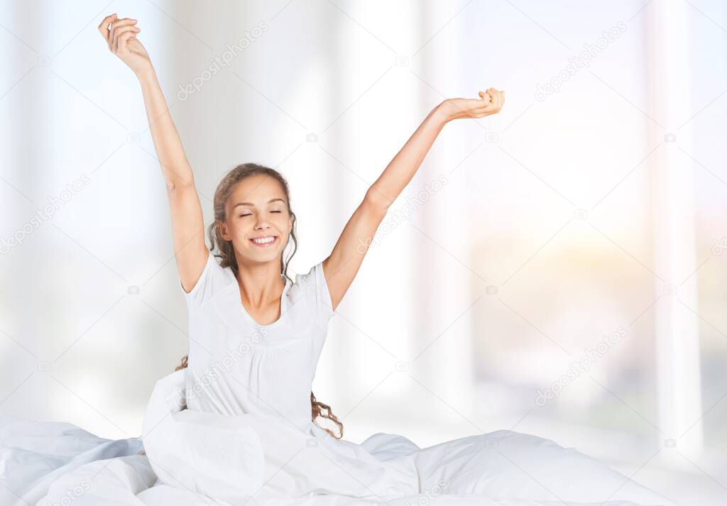 Young woman waking up in morning sitting on bed  