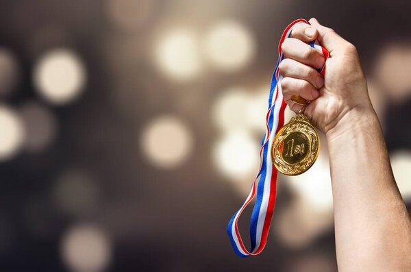 man's hand holding golden medal 