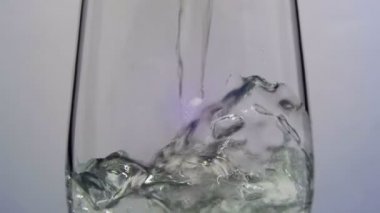 Su beyaz arka plan üzerine saydam bir cam içine dökülür. Ağır çekim