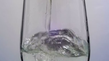 Su beyaz arka plan üzerine saydam bir cam içine dökülür. Ağır çekim
