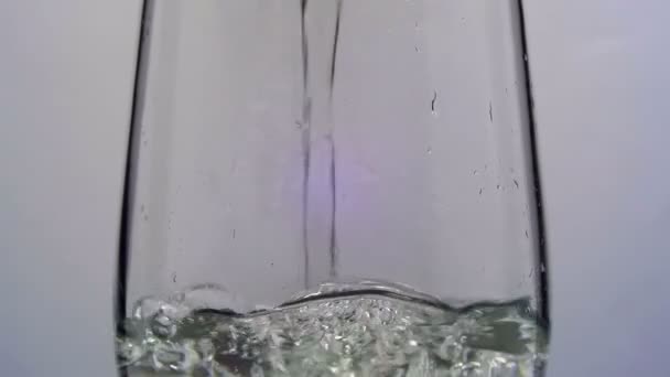 A água é derramada em um vidro transparente em um fundo branco. Movimento lento — Vídeo de Stock