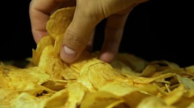 Adam ağır çekimde siyah arka plan üzerinde ahşap bir masa üzerinde elle patates cipsi alır