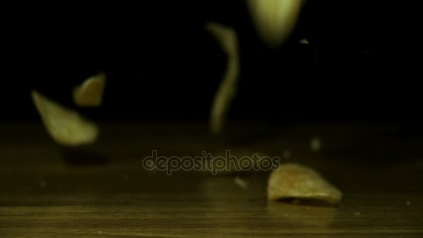 Chips de pomme de terre tombent sur une table en bois sur fond noir au ralenti — Video