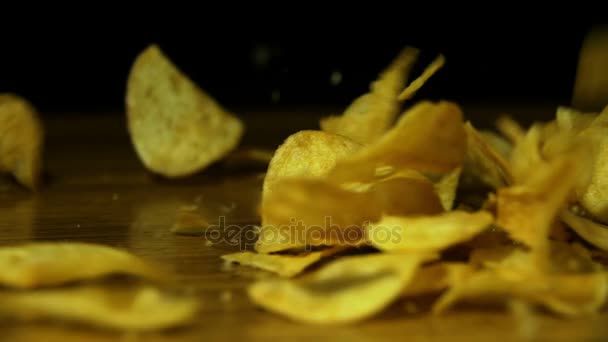 Chips de pomme de terre tombent sur une table en bois sur fond noir au ralenti — Video