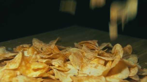 Картофельные чипсы падают на деревянный стол на черном фоне в медленном движении — стоковое видео