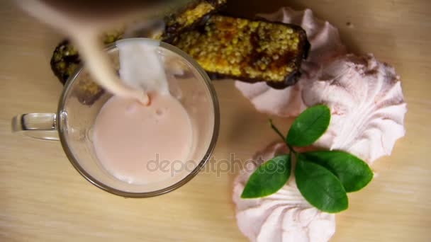 Jogurt jest wlewany do przezroczystego szkła na drewnianym stole w zwolnionym tempie — Wideo stockowe
