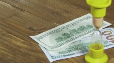 Bir ahşap masa ve kum saati düşen Doları banknot