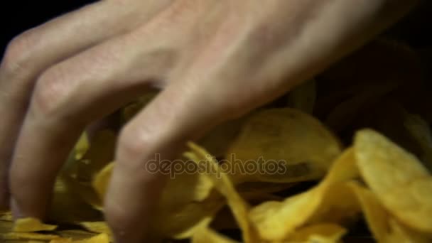 Человек берет картофельные чипсы вручную на деревянный стол на черном фоне в медленном движении — стоковое видео