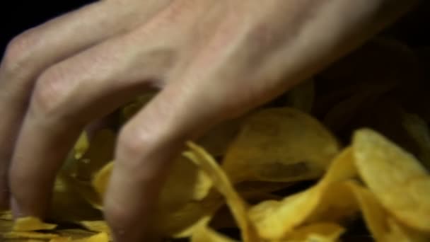 L'homme prend les chips de pommes de terre à la main sur une table en bois sur fond noir au ralenti 